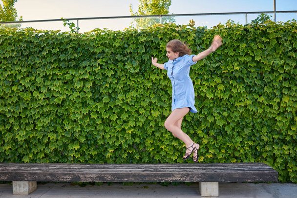 Mulher saltando de um banco para o chão. Ela está jogando em um parque ao ar livre
. - Foto, Imagem