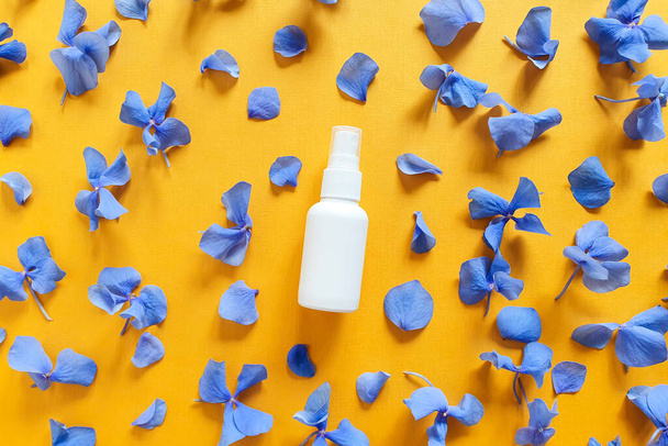 Top view and close-up of mockup  of unbranded white plastic spray bottle and petals of blue hydrangea flowers on a textured bright orange yellow background. Natural organic spa cosmetics. Flatlay. - Photo, Image
