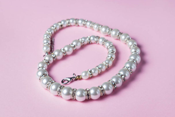 White pearl decoration on a pink background. Women's accessory. Glamorous decoration - Photo, Image