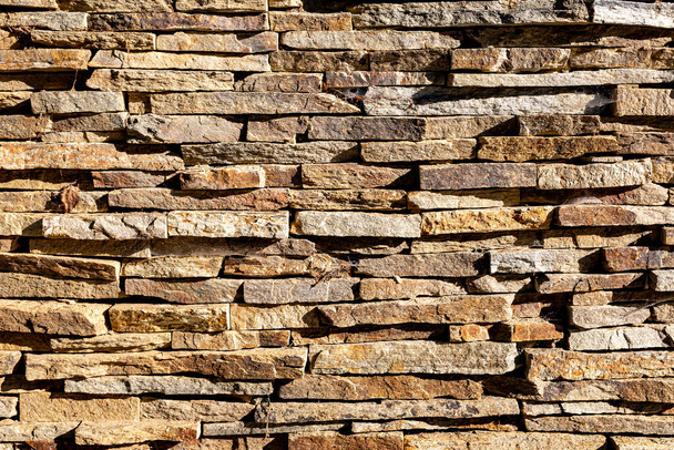 Background wall of stones. The surface of the stones is brown. Background texture. Masonry of thin vertical stones. - Foto, Bild