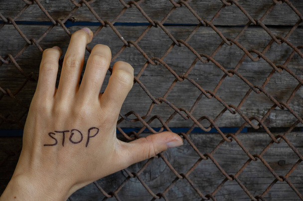 γυναικείο χέρι σε ένα πλέγμα με τη λέξη stop στα αγγλικά, οι άνθρωποι κοινωνικά προβλήματα - Φωτογραφία, εικόνα