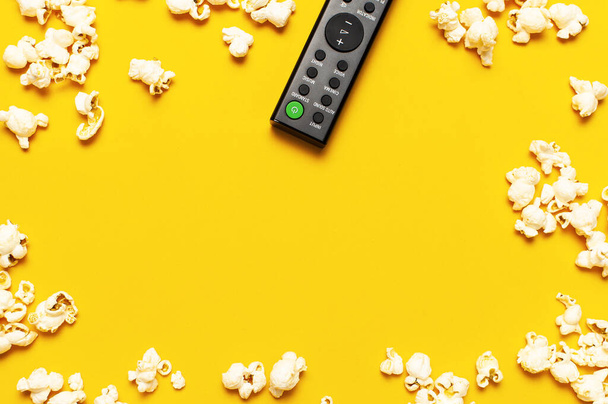Schwarze TV-Fernbedienung und Popcorn auf leuchtend gelbem Hintergrund. Minimalistischer Hintergrund mit Fernbedienung, Ansehen eines Films, einer Serie, Set-Top-Boxen, Audiosystem. - Foto, Bild