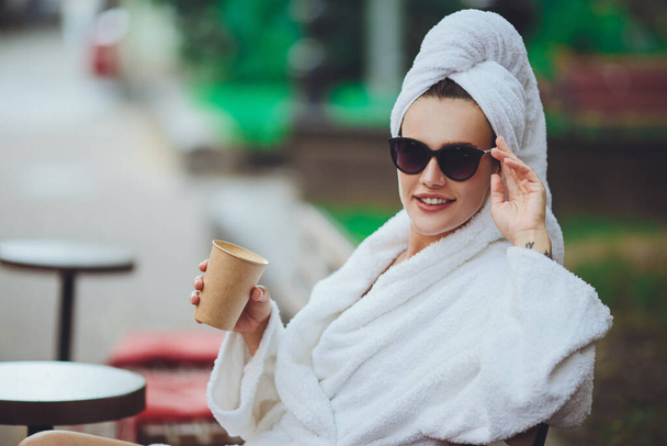 A girl in a robe and a towel on her head sits drinking coffee - Photo, image