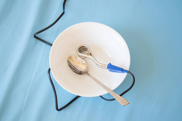 hervidor de agua en espiral para las golosinas de té en blanco plato limpio con cuchara sobre fondo azul - Foto, imagen