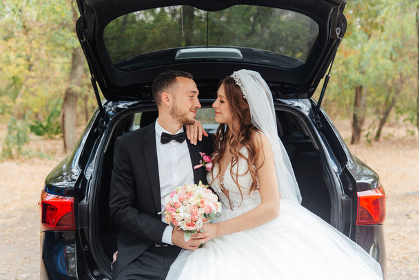 美しい豪華なカップルの結婚式の散歩、花束付きの結婚式の白いドレスの花嫁と自然の中で黒いスーツの新郎屋外 - 写真・画像