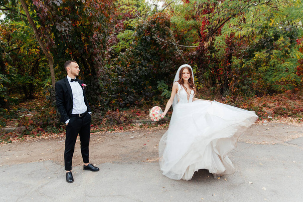 Svatební procházka krásného luxusního páru, nevěsta ve svatebních bílých šatech s kyticí a ženich v černém obleku v přírodě - Fotografie, Obrázek