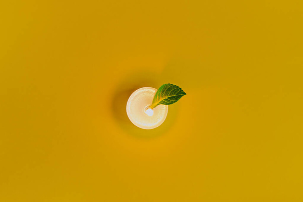 Burning candle with green leafy on colored background, elegant discreet shot - Fotoğraf, Görsel