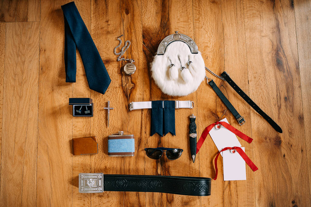 Scotsman sporrans accessoires, zakhorloge aan een ketting, stropdas, manchetknopen, kruis, riem, mes, kolf, bril, portemonnee op een glad houten oppervlak. - Foto, afbeelding