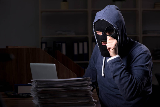 Hombre ladrón en pasamontañas en la oficina la noche
 - Foto, imagen