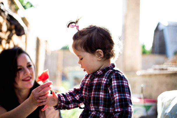 Мать и дочь гуляют по двору. Йонг дарит девочке с вьющимися волосами мак. Семейная концепция. Концепция образования. - Фото, изображение