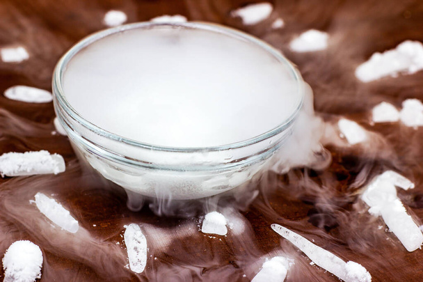 White cool dry ice (frozen carbon dioxide) with smoke effect in the glass bowl on the dark brown wooden background. - Photo, Image