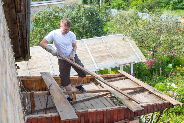dismantling the roof. The worker removes old boards from the roof, the house is being renovated. - Φωτογραφία, εικόνα