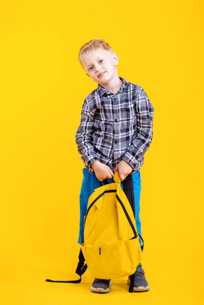 Terug naar school. Happy Six Years Old Schattige School Boy Holding Bag lachen bij de camera op gele studio achtergrond. - Foto, afbeelding