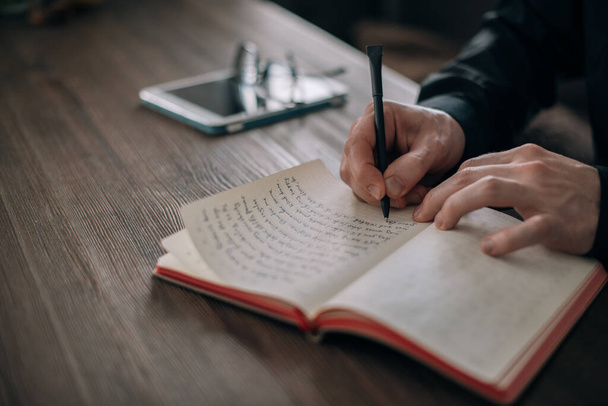 Egy fiatalember ír egy jegyzetfüzetbe az asztalnál. Kezek tollal és jegyzetfüzetekkel közelről. Újságíró, író jegyzetel, dolgozik a szövegen a munkahelyen egy világos szobában a házban - Fotó, kép