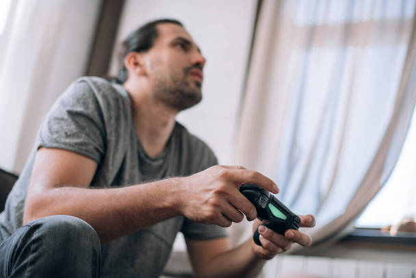 O tipo está a jogar videojogos no sofá. Um jovem com joysticks em suas mãos está entusiasticamente jogando um jogo em um console
 - Foto, Imagem