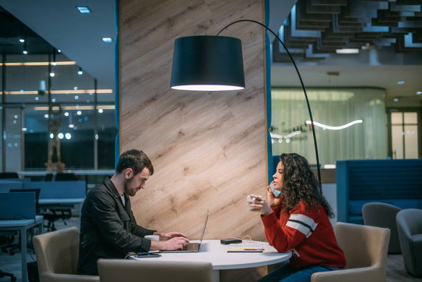Mann und Frau arbeiten abends im Coworking. Ein junger Mann mit einem Mädchen diskutiert in einem modernen Arbeitszimmer über Arbeitsfragen. Ein Team von Kollegen kommuniziert an einem Tisch in einem stilvollen Raum. - Foto, Bild