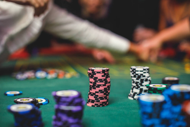 A close-up vibrant image of multicolored casino table with roulette in motion, with casino chips. the hand of croupier, mone and a group of gambling rich wealthy people in the backgroun - Foto, Imagem