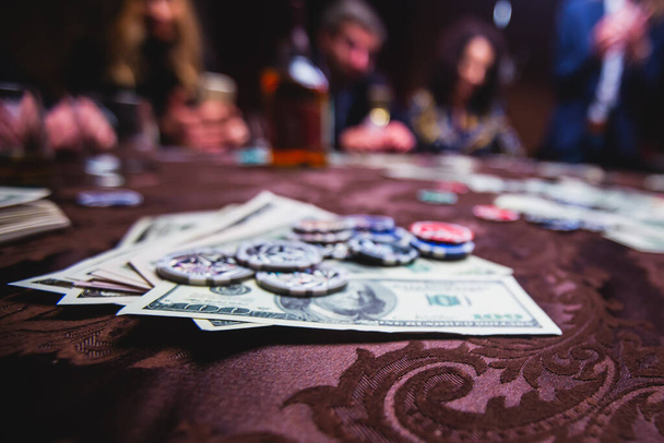 View of poker table with pack of cards, tokens, alcohol drinks, dollar money and group of gambling rich wealthy people playing poker - Foto, Imagen