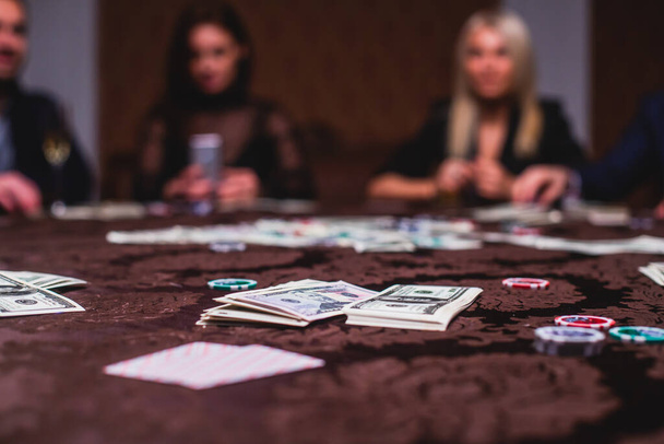 View of poker table with pack of cards, tokens, alcohol drinks, dollar money and group of gambling rich wealthy people playing poker - Photo, image