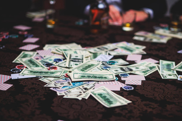 View of poker table with pack of cards, tokens, alcohol drinks, dollar money and group of gambling rich wealthy people playing poker - Fotografie, Obrázek