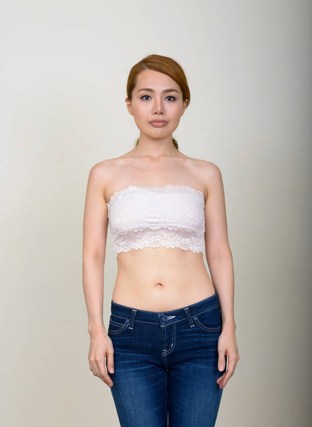 Studio shot of young beautiful Japanese woman wearing bra against white background - Foto, Imagem