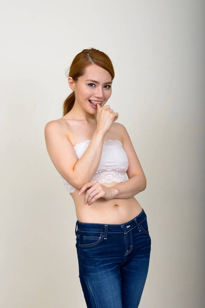 Studio shot of young beautiful Japanese woman wearing bra against white background - Foto, imagen