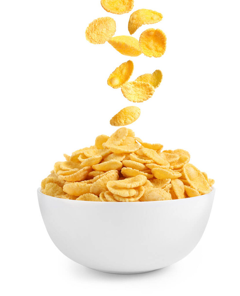 Tasty crispy corn flakes falling into bowl on white background. Breakfast cereal - Фото, изображение
