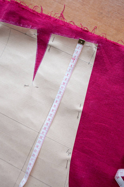 A paper pattern of trousers and a centimeter ribbon lie on a red cloth on the table - Photo, Image