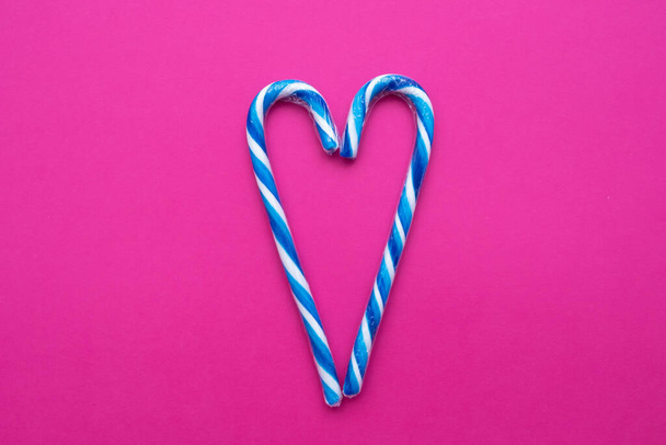 bastones de caramelo multicolores en forma de corazón sobre un fondo rosa, espacio de copia - Foto, imagen