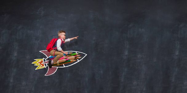 Portret van een jong kind op een raket met een tas. Hij speelt thuis. Kind vliegt op een getrokken raket in de onderwijsruimte. Verbeelding, idee en creatief. Kopieer ruimte voor je tekst. winnaar en leider. - Foto, afbeelding