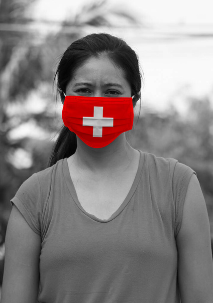 Флаг Швейцарии на гигиенической маске. Черно-белая азиатская женщина в маске предотвращает развитие микробов. концепция вирусной короны или ковида 19 или защиты крошечных частиц. - Фото, изображение