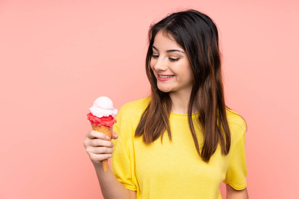 Young brunette woman holding a cornet ice cream over isolated pink background with happy expression - 写真・画像
