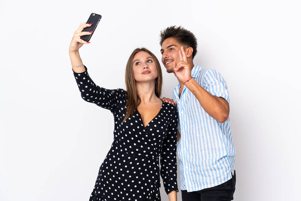 Young caucasian couple isolated on white background making a selfie with the mobile - Valokuva, kuva
