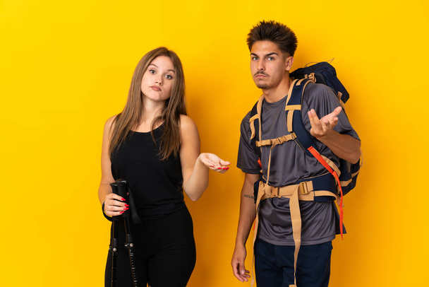 Junge Bergsteiger-Paar mit einem großen Rucksack isoliert auf gelbem Hintergrund unglücklich und frustriert über etwas, weil sie etwas nicht verstehen - Foto, Bild