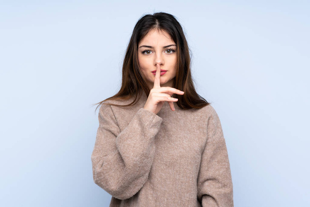 Mladá brunetka žena nosí svetr přes izolované modré pozadí ukazující znamení mlčení gesto dát prst do úst - Fotografie, Obrázek