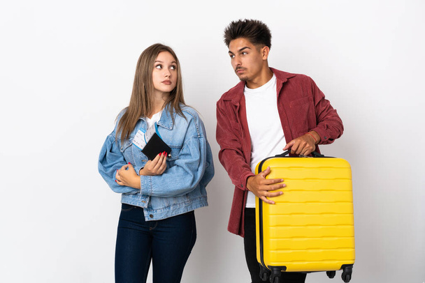 Traveler couple holding a suitcase isolated on blue background making doubts gesture while lifting the shoulders - Фото, зображення