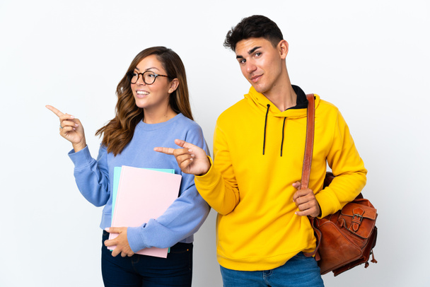 Junges Studentenpaar isoliert auf weißem Hintergrund zeigt mit dem Finger zur Seite in seitlicher Position - Foto, Bild