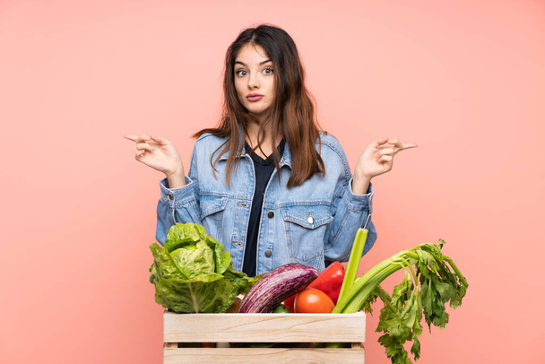 Mladá farmářka drží košík plný čerstvé zeleniny a ukazuje na laterály, které pochybují - Fotografie, Obrázek