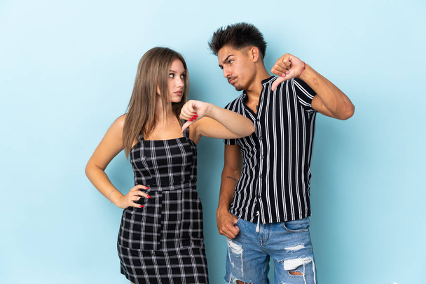 Teenager caucasian couple isolated on blue background showing thumb down sign with negative expression - Фото, изображение