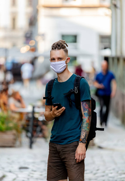 νεαρός με μάσκα προσώπου και dreadlocks χρησιμοποιεί το κινητό τηλέφωνο στο δρόμο - Φωτογραφία, εικόνα