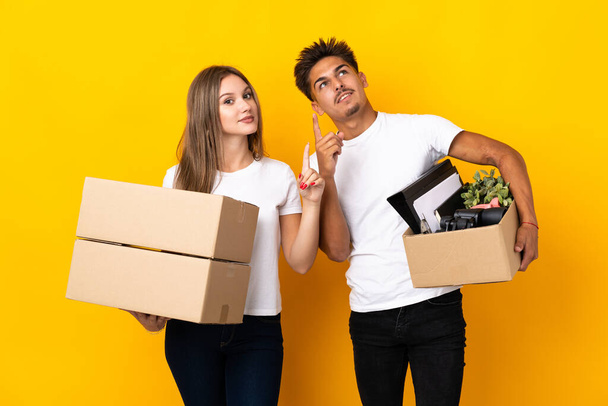 Teenager couple moving in new home among boxes isolated on blue background pointing with the index finger a great idea - Photo, Image