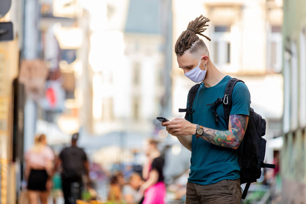fiatal srác arcmaszk és raszta használ mobiltelefon az utcán - Fotó, kép