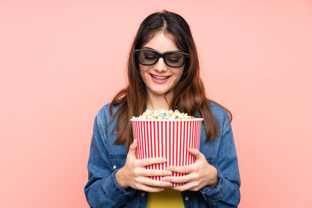 Giovane donna bruna su sfondo rosa isolato con occhiali 3d e tenendo un grande secchio di popcorn - Foto, immagini
