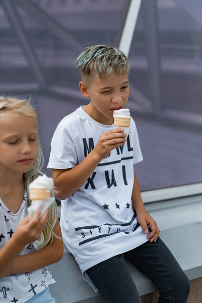 Two happy children, brother and sister, sibling interaction. Brother and sister dressed in casual eating ice cream in a cone. - Fotó, kép