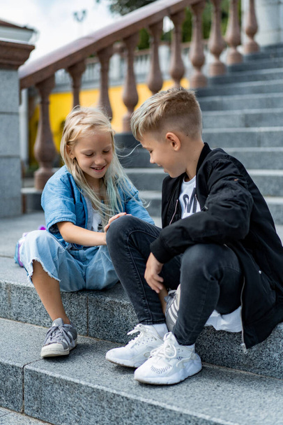 Two happy children, brother and sister, sibling interaction. Brother and sister dressed in casual on the steps in the city center. - Foto, Bild