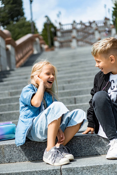 Two happy children, brother and sister, sibling interaction. Brother and sister dressed in casual on the steps in the city center. - Foto, immagini