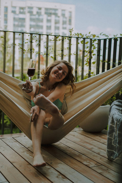 A young woman on a private terrace of a country house in a hammock is resting, a glass of champagne lambrusca in her hand, summer chill. - Fotografie, Obrázek