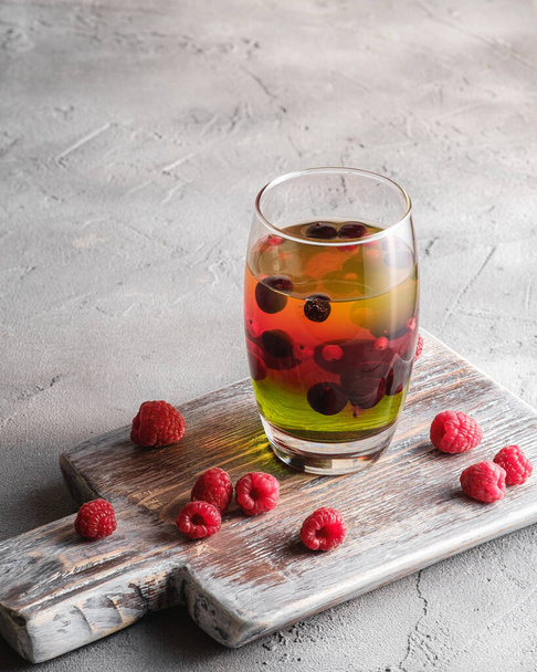 Желейний десерт з ягодами в склі на старій дерев'яній обробній дошці, солодкий барвистий шаруватий пудинг, кам'яний бетонний фон, вид на кут
 - Фото, зображення