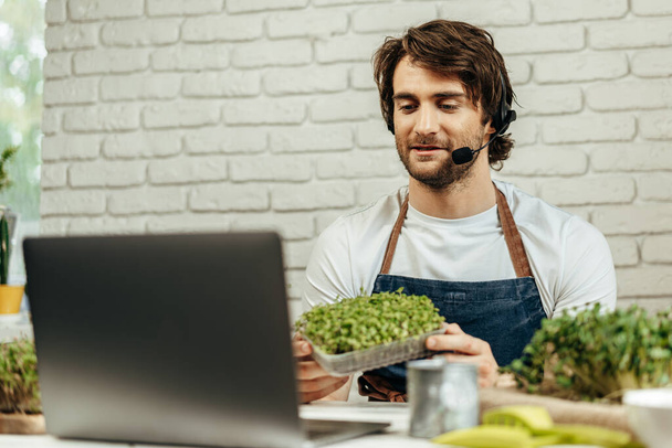 Handsome bearded man sells plant sprouts and seedlings online using laptop - Φωτογραφία, εικόνα