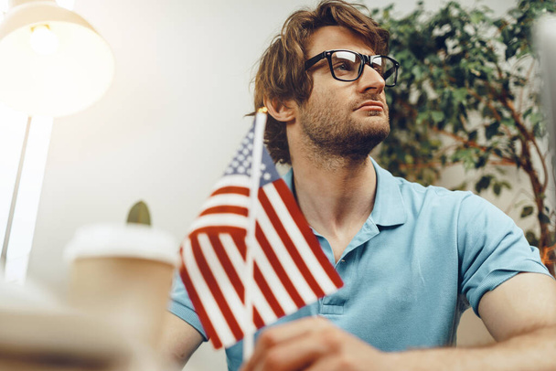 Young bearded businessman sitting at table with laptop and american flag - Foto, immagini